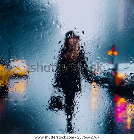 View through glass window with rain drops on blurred  silhouette of a girl on a city street after rain and colorful neon bokeh city lights, night street scene. Focus on raindrops on glass Royalty-Free Stock Photo #2396642767