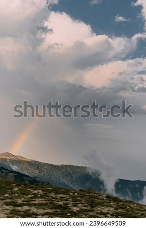 Landscape with a rainbow in a stormy sky among mountains and low clouds