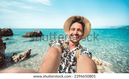 Happy man taking selfie with smart mobile phone outside - Cheerful tourist enjoying summer vacation at the beach - Travel life style and technology concept Royalty-Free Stock Photo #2396650801