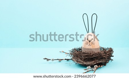 Easter bunny or rabbit sitting in a bird nest, willow branches, wooden egg, spring holiday, brown and blue color