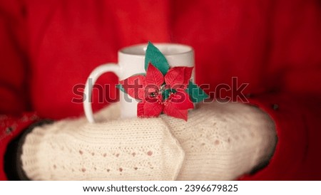 Photo of a white mug decorated with a red poinsettia held by hands in white lace mittens. A man holding a mug in a red jacket. The face is not visible.