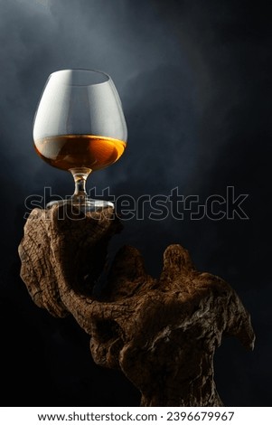 Snifter of brandy on a old wooden snag. Black background with copy space. Selective focus.