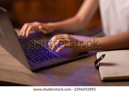 A businesswoman has a job in the office or works at home remotely, sits at the table, uses a copybook for writing notes and laptop for typing text on the keyboard. Close up with no face focused. Royalty-Free Stock Photo #2396692895