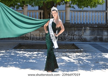 Pretty young woman winner of a beauty pageant dressed in a green sequined dress. Young woman wears diamond crown and winner's sash and poses for photo. Fashion and beauty concept Royalty-Free Stock Photo #2396697019