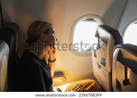 Passenger woman is flying in plane. Girl sitting in airplane looking out window going on trip vacation travel. Traveling female inside plane enjoying flight. Traveling girl Royalty-Free Stock Photo #2396708399