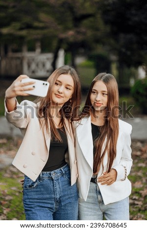 Two young women taking a selfie with a smart mobile phone outdoors - happy beautiful female friends smiling at the camera outdoors - lifestyle concept with cheerful girls enjoying outdoor recreation.