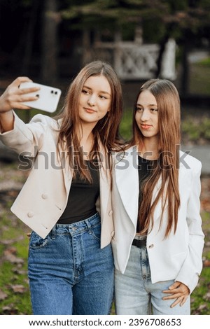 Two young women taking a selfie with a smart mobile phone outdoors - happy beautiful female friends smiling at the camera outdoors - lifestyle concept with cheerful girls enjoying outdoor recreation.