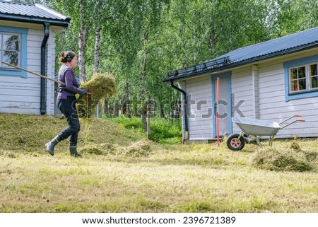 Mature women carrying fresh cut grass to garden wheelbarrow - summer gardening work at summer cottage. Side photo