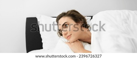 Close up portrait of beautiful brunette woman, waking up in her bed, looking at alarm clock, staring aside with smiling dreamy face.