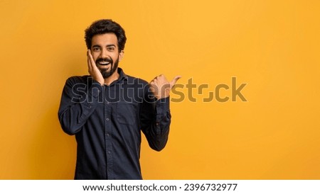 Amazing Offer. Excited Shocked Indian Guy Touching Face And Pointing Aside At Copy Space, Amazed Eastern Male In Black Shirt Demonstrating Free Place For Advertisement, Standing On Yellow Background