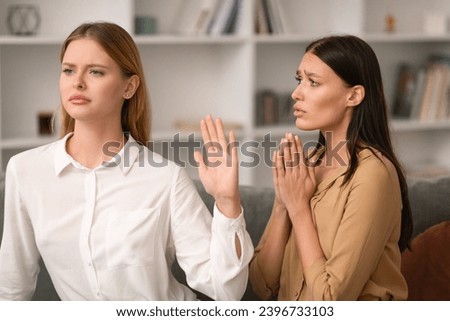 Woman Saying No and Gesturing Stop In Refusal To Friend Begging For Favor Or Forgiveness After Quarrel, Sitting On Couch In Modern Living Room Interior. Friendship Relationship Problems Royalty-Free Stock Photo #2396733103