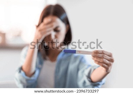 Infertility concept. Depressed unrecognizable lady showing negative pregnancy test at home interior. Selective focus on test result as depressed woman shows it to camera. Shallow depth Royalty-Free Stock Photo #2396733297