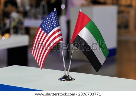 Two small table flags of the USA and the United Arab Emirates together at some event or fair, as a symbol of cooperation between the two states