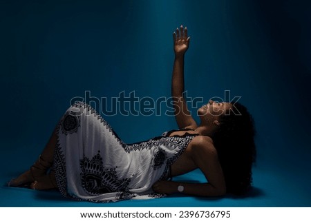 Beautiful young woman with curly hair lying on the floor looking up. Isolated on blue background.