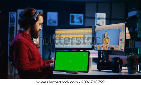 Green screen tablet on desk in photography studio next to photo editor color correcting images in retouching software. Photographer selecting best pictures for editorial content next to mockup device