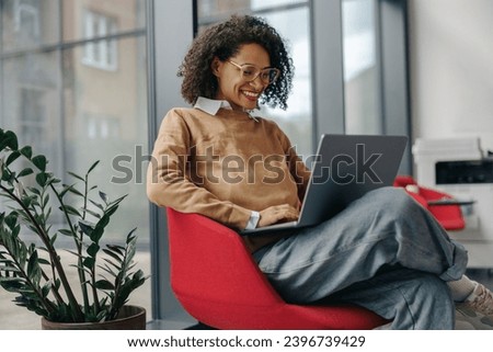 Pretty female freelancer working on laptop while sitting on modern coworking background