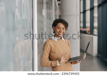 Smiling female entrepreneur using laptop while standing on office background and looks camera
