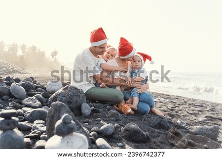 Lifestyle family portrait on ocean beach in Christmas Santa Claus Red Hats Caps. Christmas or New Year vacation and holidays. Family with kids spending time together outdoors.