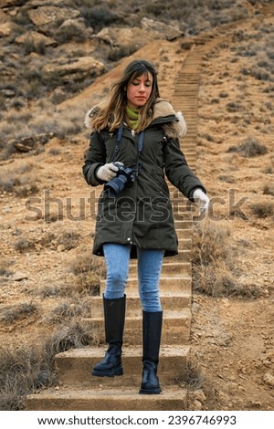 Young woman, camera in hand, wandering Bárdenas Reales desert in chilly autumn.