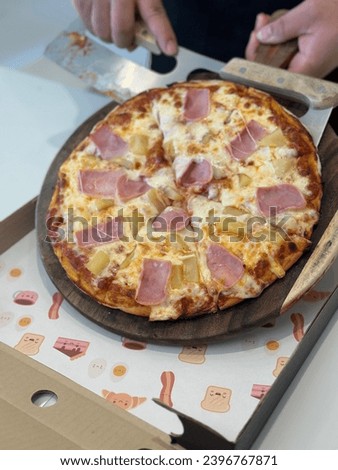 Hawaiian Pizza on wooden plate. Closeup chef cuts freshly prepared pizza slices. Hand of chef baker in white uniform cutting pizza at kitchen. Pizza picture free space for text.  