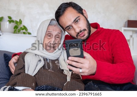 male showing smart phone to his muslim grandmother