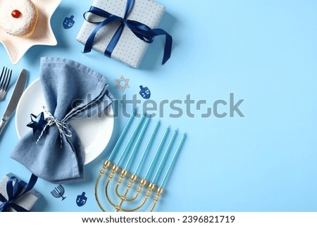 Happy Hanukkah concept. Jewish religious holiday celebration. Flat lay composition with menorah, plate with napkin and cutlery, jelly doughnut, gift boxes on blue background.