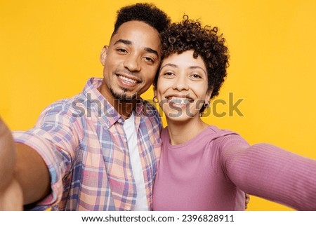 Close up young couple two friends family man woman of African American ethnicity wear purple casual clothes together do selfie shot pov on mobile cell phone isolated on plain yellow orange background
