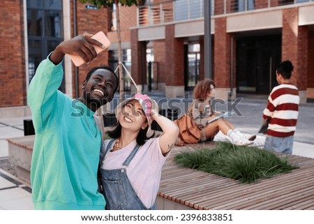 Waist up portrait multiethnic young couple taking selfie photo together via phone in city street and smiling, copy space