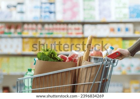 Female customer buying groceries at the supermarket, she is pushing a full shopping cart Royalty-Free Stock Photo #2396834269