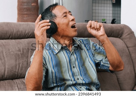 Asian senior man feeling happy enjoy listening to music with headphones on sofa at home