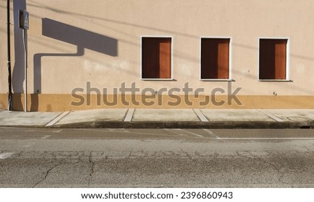 Closed window blinds on  plaster facade with pedestrian crossing sign on the left. Concrete sidewalk and street in front. Urban background for copy space.