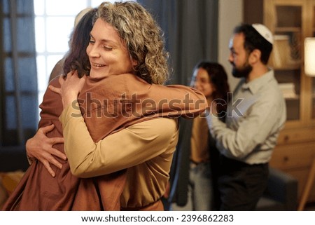 Two happy women in quiet luxury attire embracing each other in the corridor against mature man in kippah and youthful girl Royalty-Free Stock Photo #2396862283