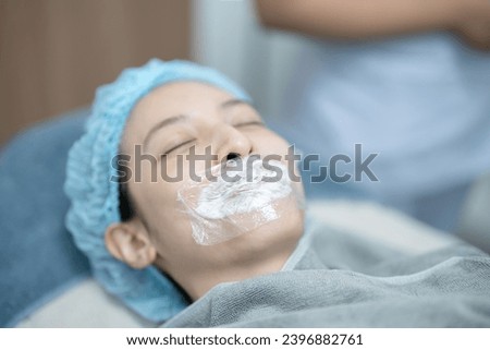 Esthetician applying numbing cream on patient's lips before injects filler.