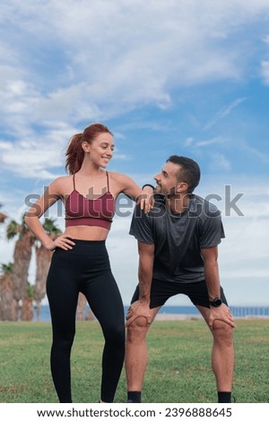 Vertical photo. Young sporty couple male and female resting exhausted with a hard training enjoying wellbeing and healthy lifestyle outdoors. Caucasian man and woman in sportswear relaxing and smiling