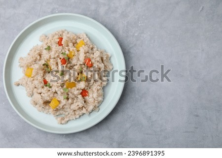 Delicious barley porridge with vegetables and microgreens on gray table, top view. Space for text Royalty-Free Stock Photo #2396891395