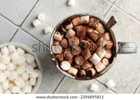 Delicious hot chocolate with marshmallows, cocoa powder and spoon in cup on tiled table, top view