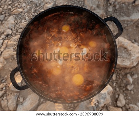 Sizzling shakshuka in a cast iron pan, traditional Middle-Eastern dish, cooked outdoors. Dawn in Mitzpe Ramon. Eggs in tomatoes with pappers.