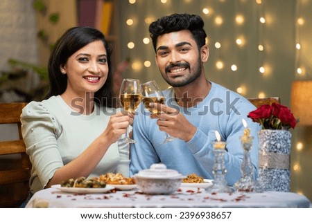 Happy smiling couple champagne wine in hands by looking at camera during candle light dinner at home - concept of romantic couple, dating and valentine's day Royalty-Free Stock Photo #2396938657