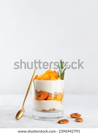 Parfait in a glass with persimmon, rosemary, pecan, whipped cream, biscuit and spoon. Vegan, sugar, gluten and lactose free. Fruit dessert, cheesecake, trifle, mouse in a glass. Vertical orientation. Royalty-Free Stock Photo #2396942791