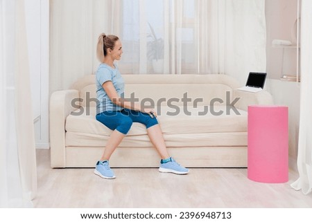 Attractive healthy sporty woman using laptop and watching online training tutorial, Virtual training: A girl engages in home exercise, following an online course by the sofa