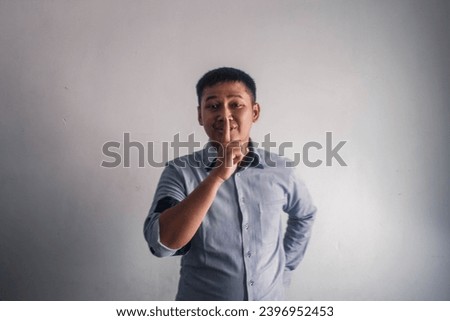 Handsome Asian young man wearing blue striped shirt looks gesturing no noise, business and finance