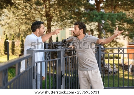 Angry neighbours having argument near fence outdoors Royalty-Free Stock Photo #2396956931