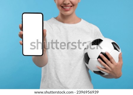 Happy sports fan with soccer ball and smartphone on light blue background, closeup