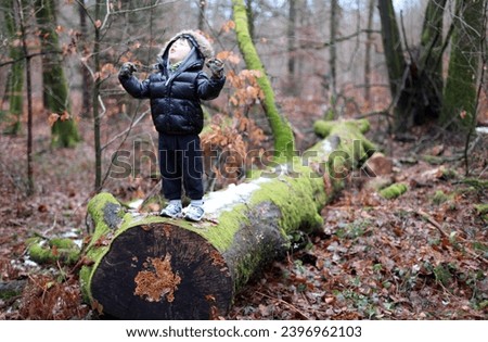 Exterior natural view photo of a young kid child children male boy shouting like a wolf to teh moon on a fallen fall dead tree trunk in a forest during autumn winter by day to express power powerful