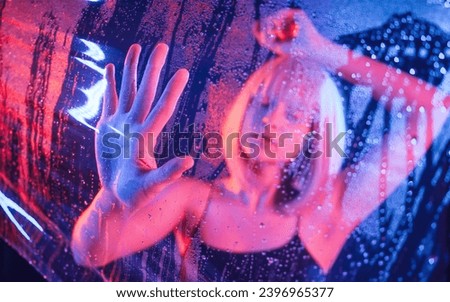 Hands are on the surface. Stylish woman with white hair is behind wet transparent plastic sheet.