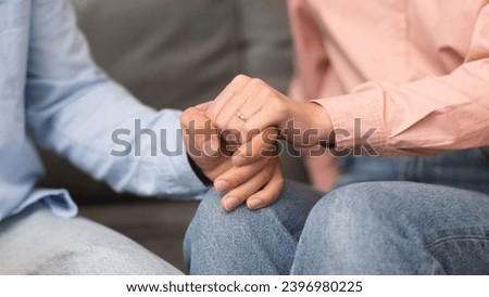 Marriage, love and unity. Closeup of young couple's hands tenderly holding each other, woman wearing ring indoor. Intimate gesture of clasped hands. Bond and affection between partners. Panorama Royalty-Free Stock Photo #2396980225