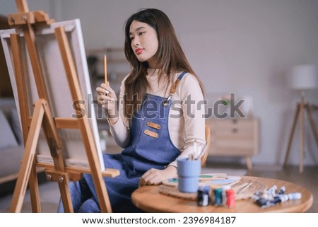 Young asian female artist holding pencil to measuring proportion on the canvas for painting artwork.