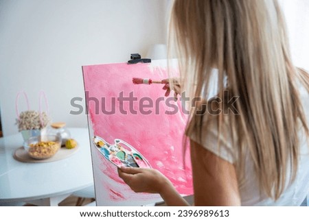 Young woman artist with palette and brush painting abstract pink picture on canvas at home. Back view. Art and creativity concept. High quality photo