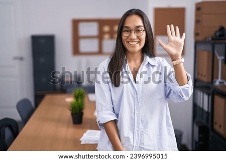 Young hispanic woman at the office showing and pointing up with fingers number five while smiling confident and happy. 