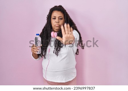 Plus size hispanic woman wearing sportswear and headphones doing stop sing with palm of the hand. warning expression with negative and serious gesture on the face. 